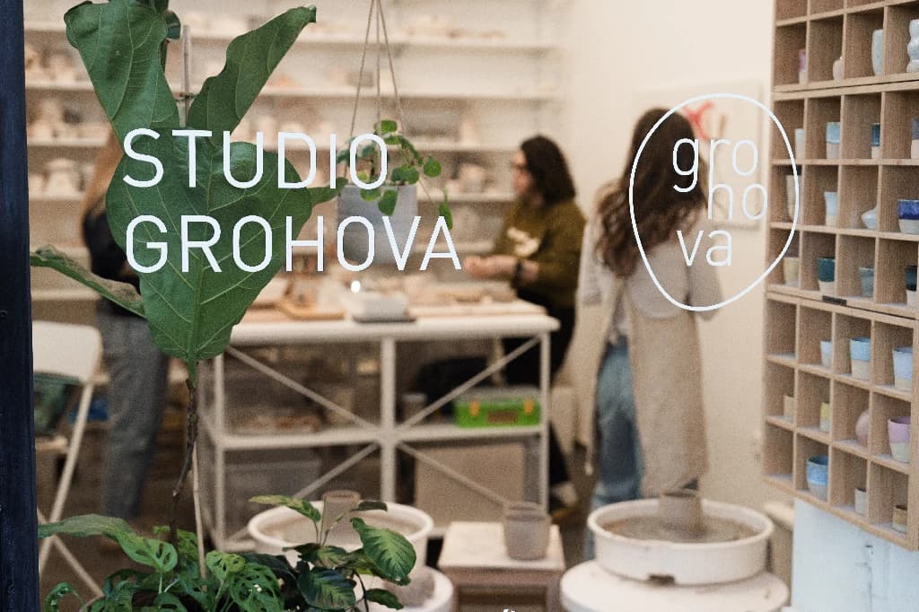Lidé tvoří keramiku ve Studiu Grohova, pohled přes výlohu s názvem studia